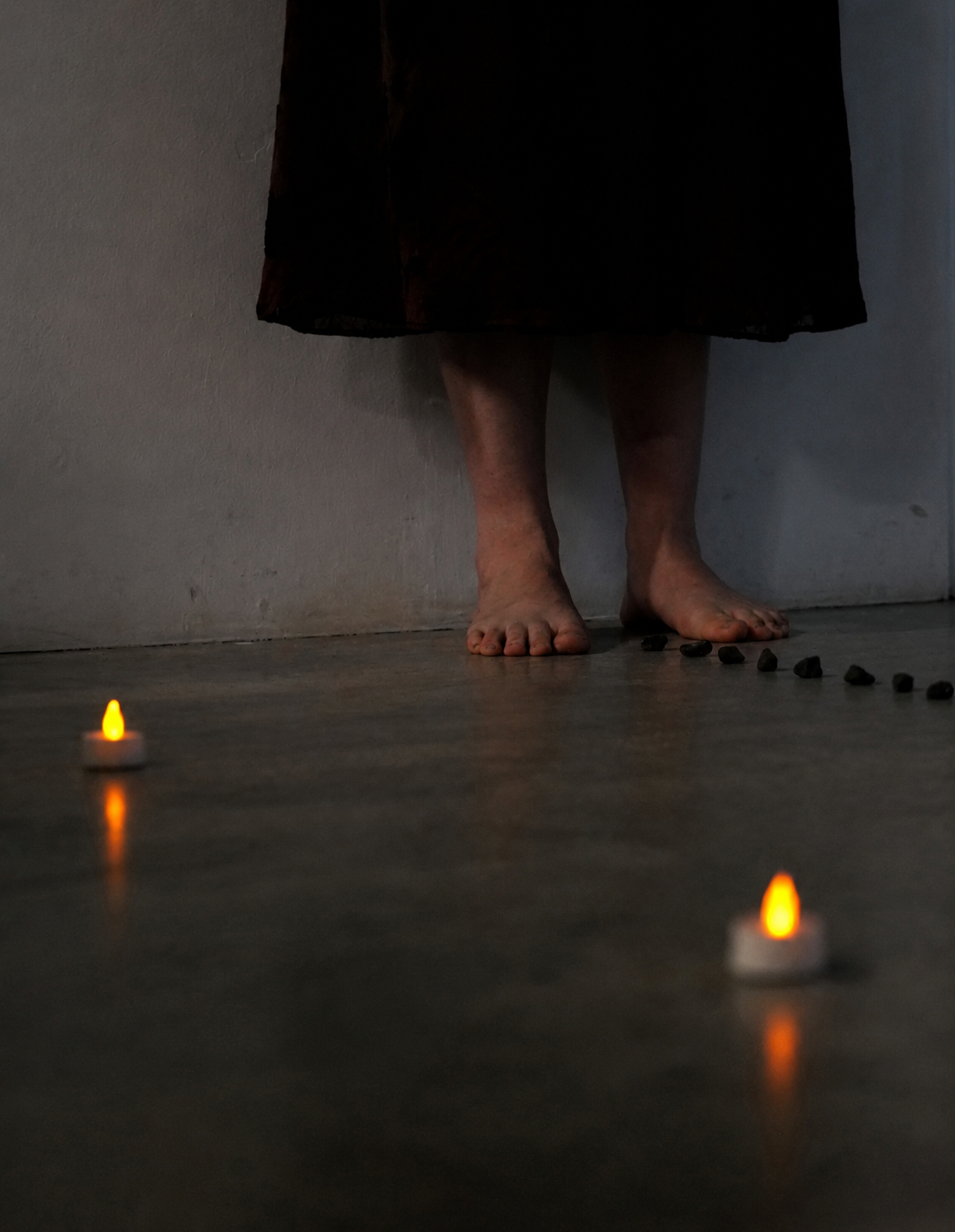 Bare feet among candles and a line of stones